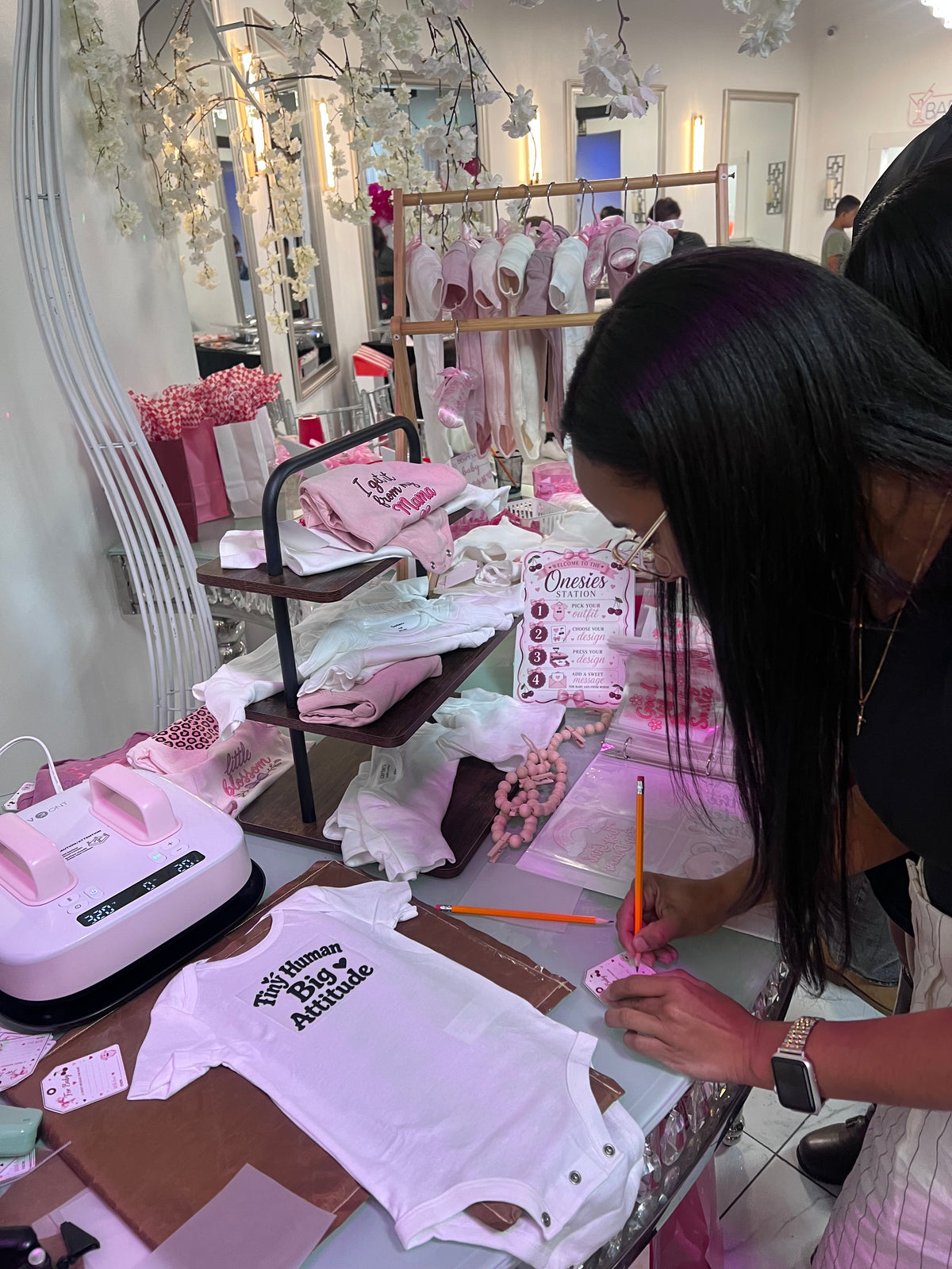 Guest customizing a baby onesie at a pink-themed on-site pressing station.